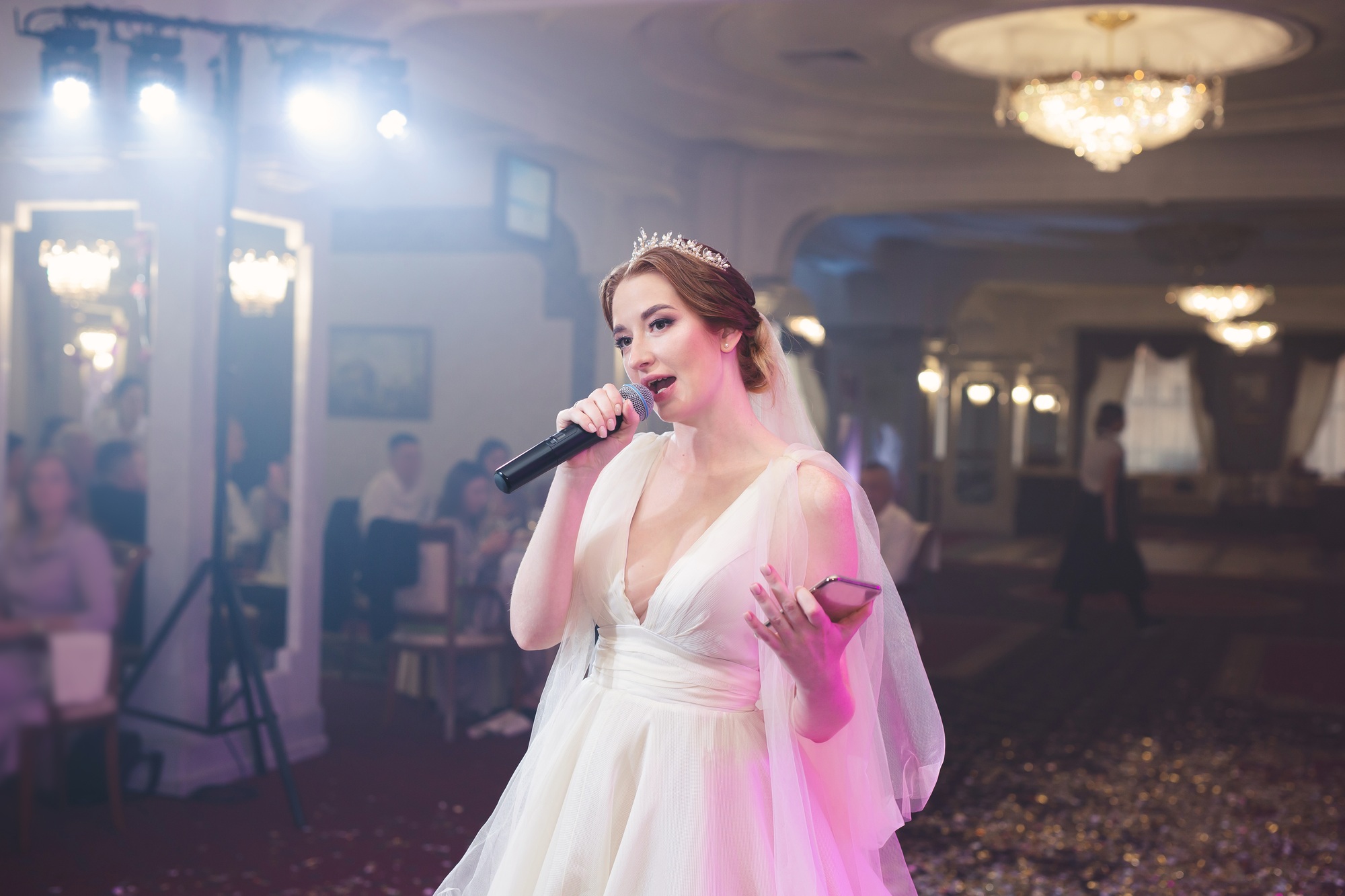 Beautiful bride in a wedding dress holds a microphone and sings at a banquet.