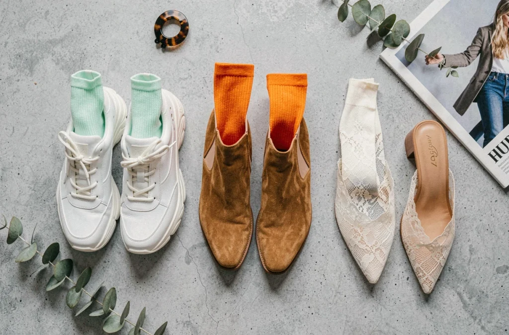 Flat lay éditorial de trois associations chaussettes et chaussures tendance : sneakers blanches, bottines Chelsea et mules pointues sur fond béton gris
